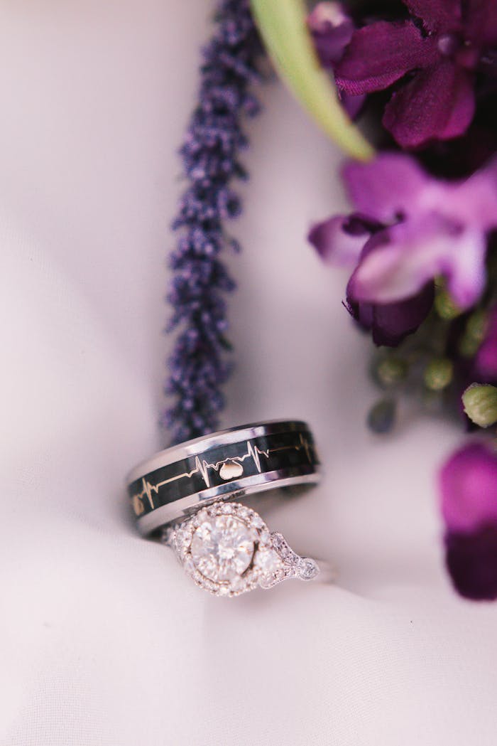 contact-img Close-up of wedding rings with purple floral background, showcasing elegant design.